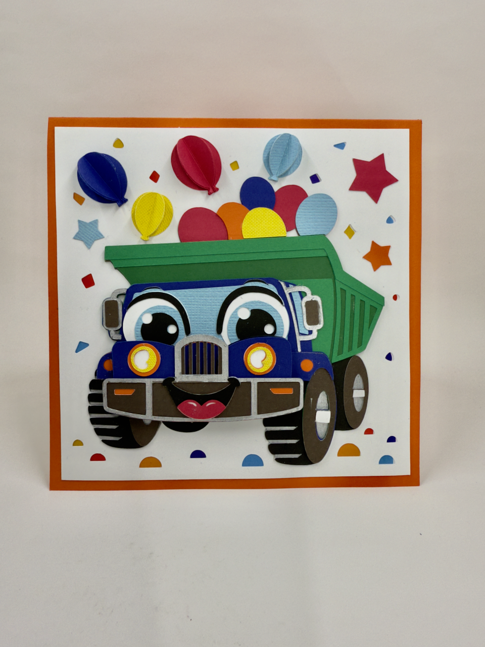 A colorful birthday card featuring a cartoon dump truck with balloons and birthday decorations.