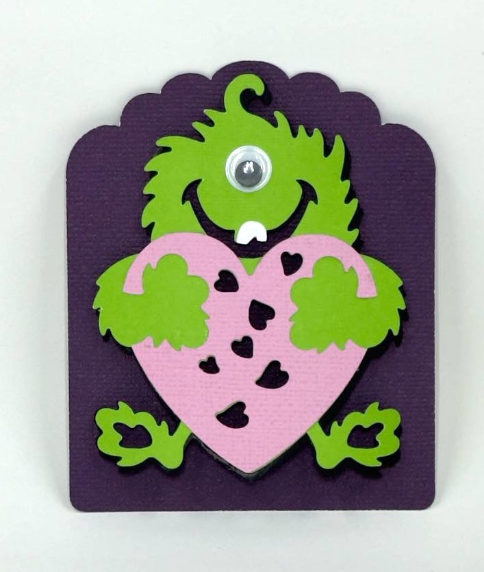 A colorful Valentine's Day card featuring a green monster with a pink heart, crafted for children.