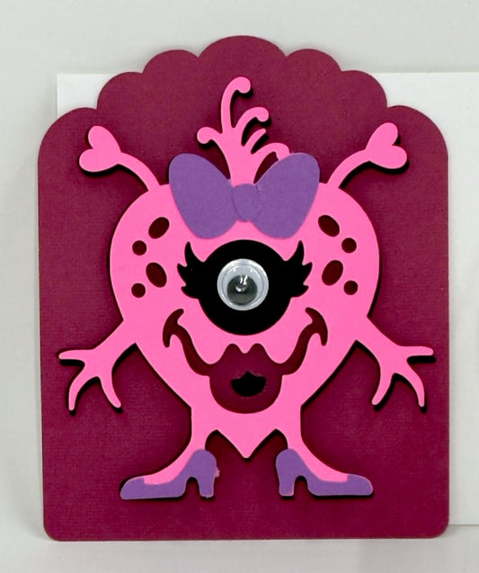 A colorful Valentine's Day card featuring a pink monster with a purple eye and bow, crafted for children.