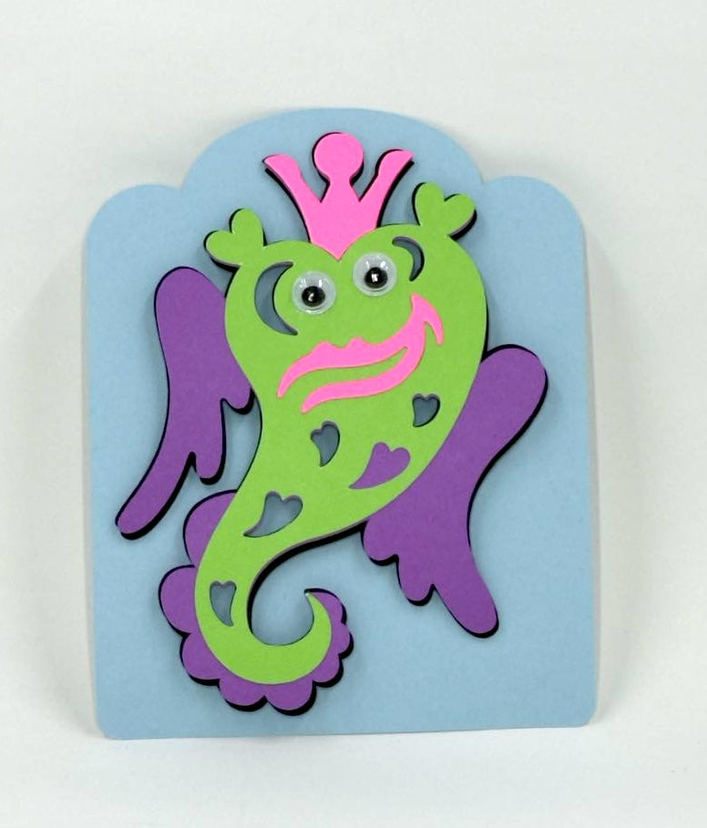 A colorful Valentine's Day card featuring a green monster with a purple fines, crafted for children.